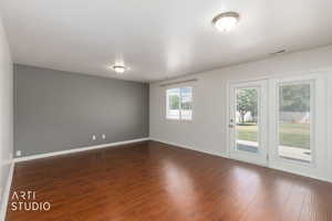 Spacious room featuring rich wood-finish flooring, a neutral accent wall, and white trim