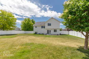 Expansive backyard featuring a large grass area, mature trees, and white privacy fencing