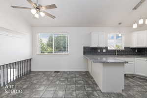 Kitchen area featuring a peninsula with a granite-style countertop, white cabinetry, dark grey subway tile backsplash, and a stainless steel sink with a gooseneck faucet