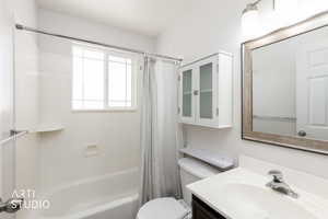 Bathroom featuring a built-in tub with a window, vanity with integrated sink, framed mirror, and wall-mounted storage cabinet