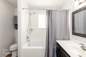 Bathroom featuring a white tub and shower combination with chrome fixtures, a window above the tub, a vanity with a white countertop and dark wood cabinetry, and a framed mirror