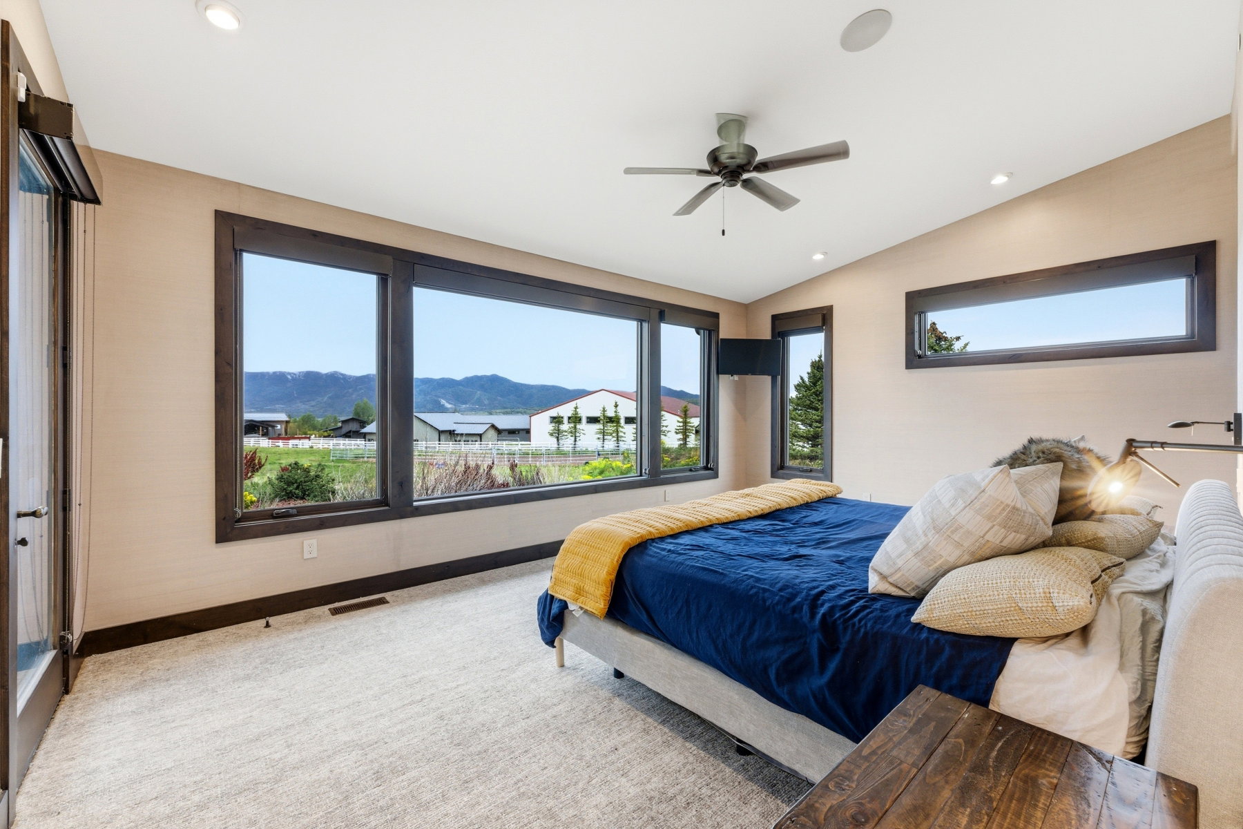 Spacious room featuring a wall of expansive windows with dark wood trim, light beige walls, recessed lighting, and a ceiling fan