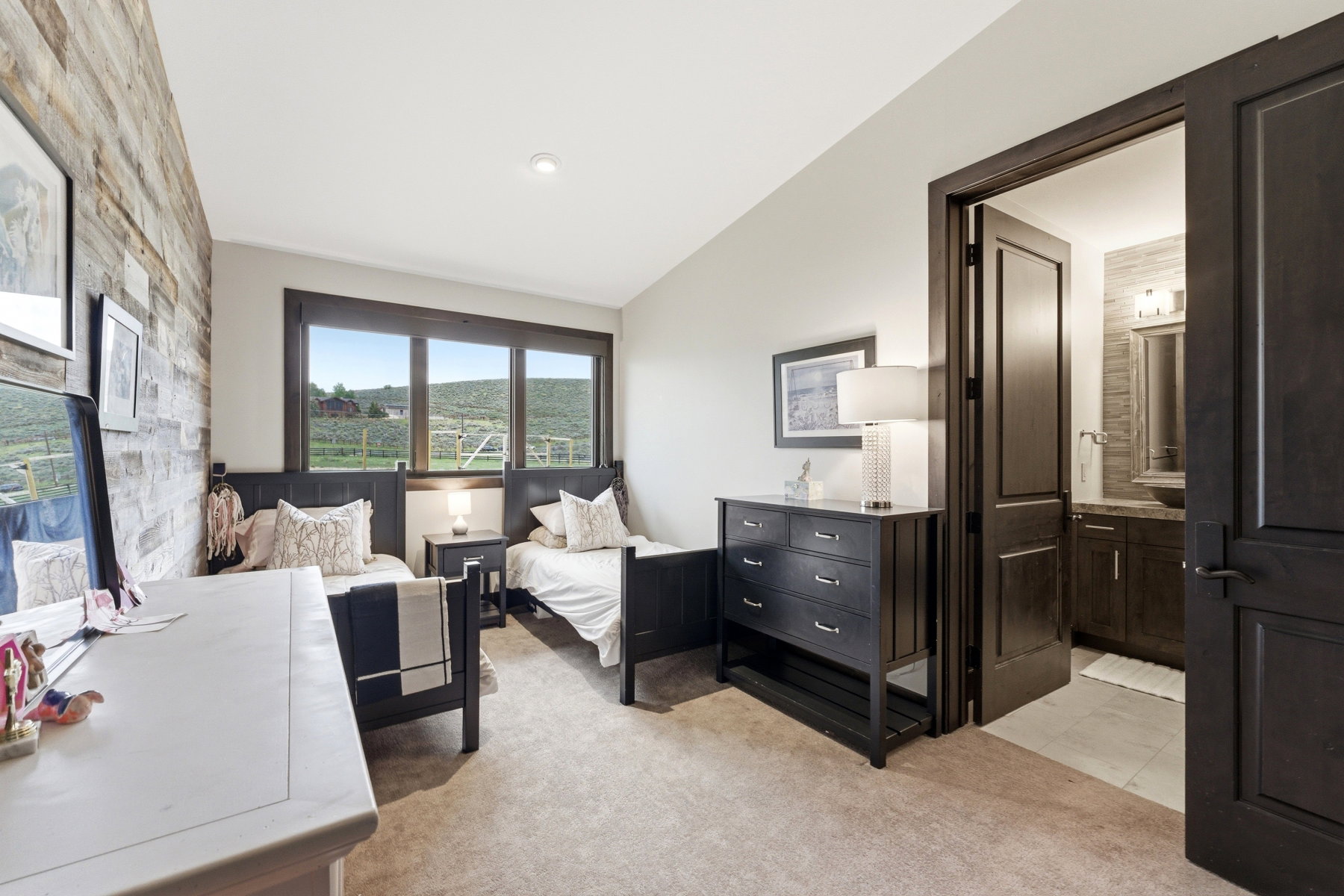 Bedroom featuring a reclaimed wood accent wall, broad windows framing a rural landscape, and plush carpet flooring