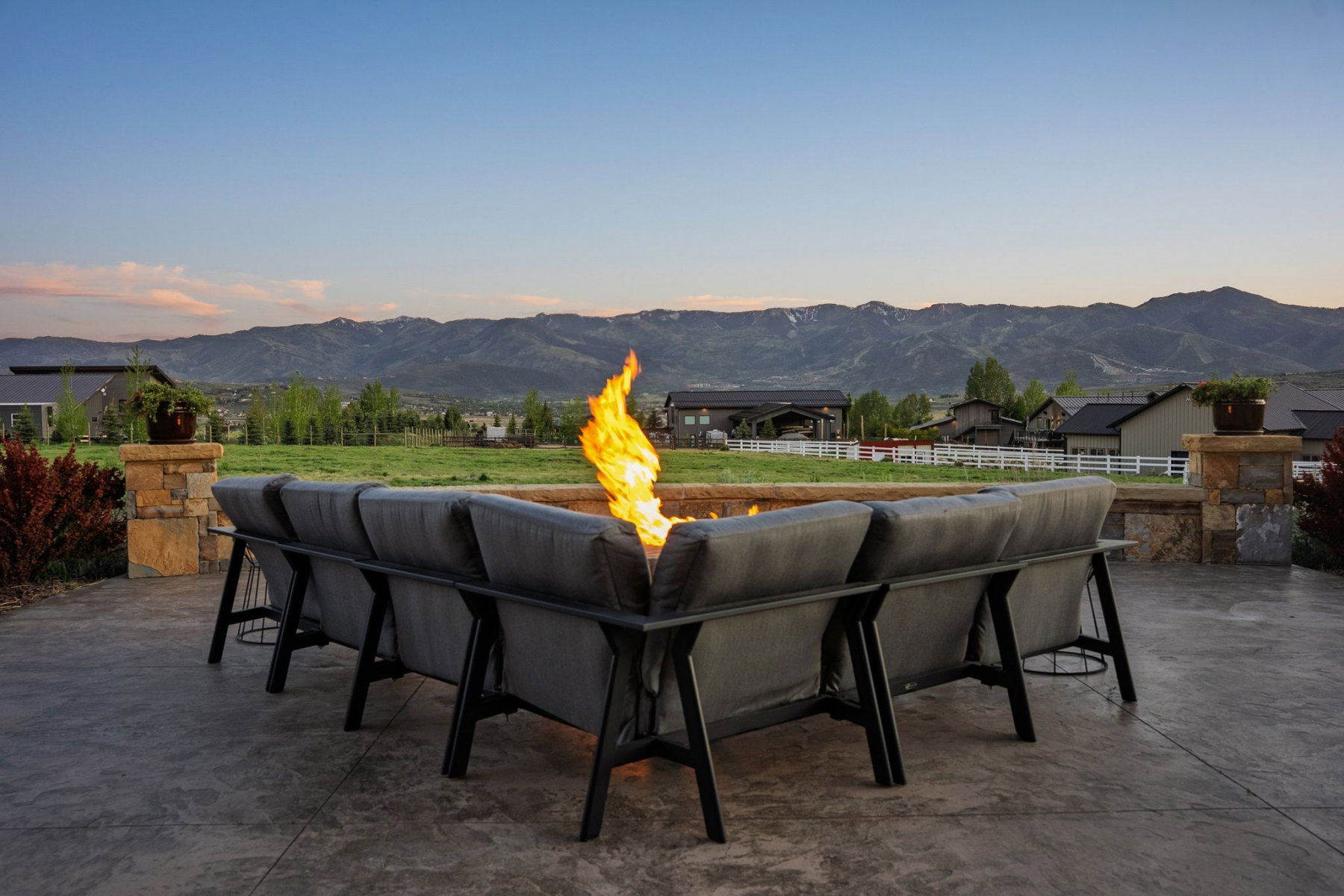 Stamped concrete patio with a built-in fire pit, stone pillar accents, and a large open field