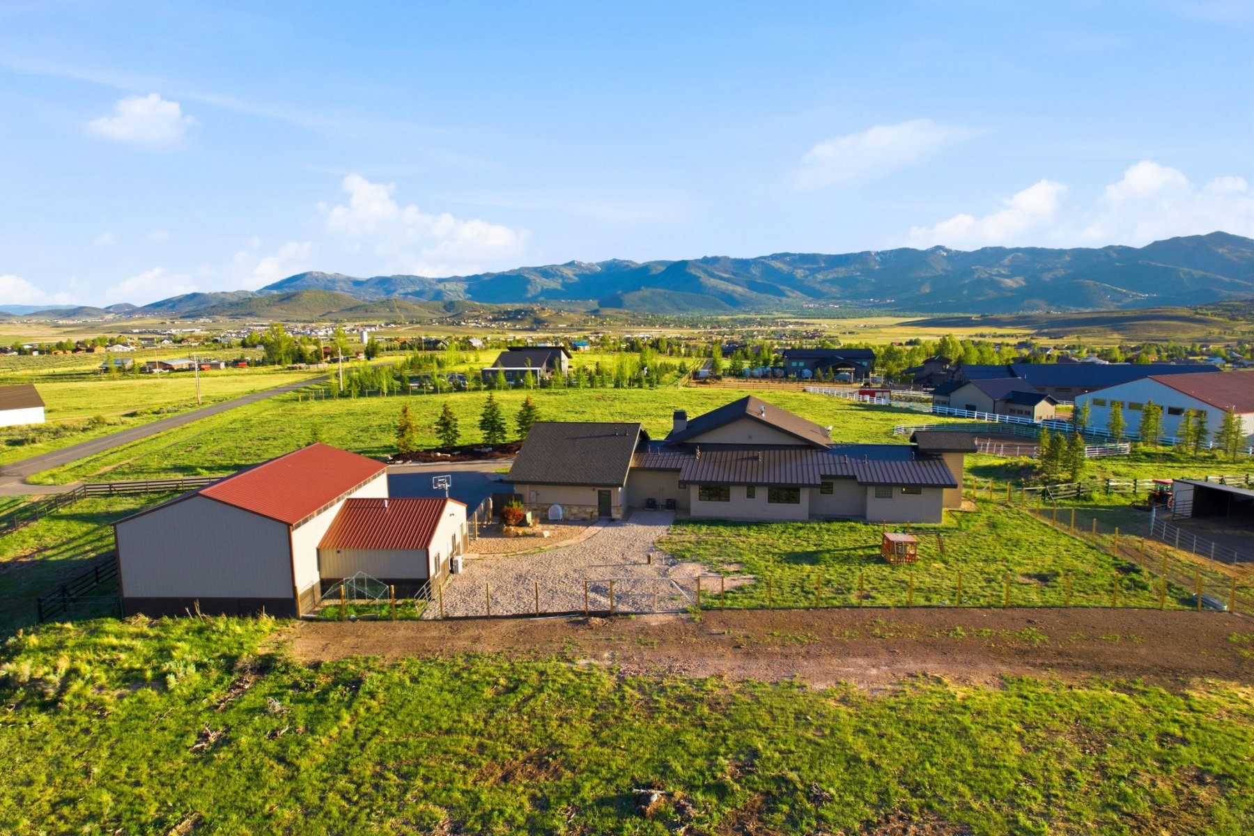 Expansive property featuring a contemporary residence, a large barn with a red roof, a separate outbuilding, and fenced pasture areas