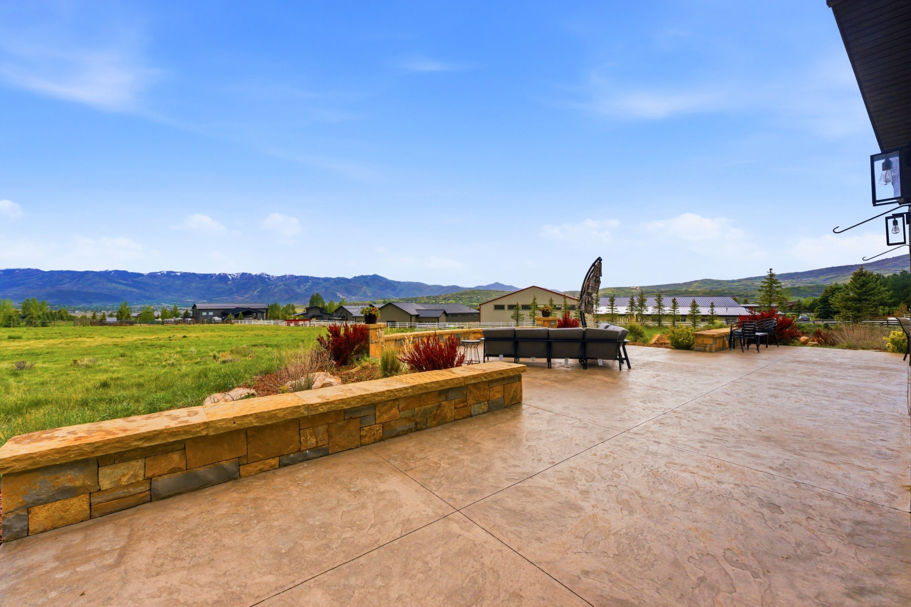 Expansive stamped concrete patio featuring a stone veneer retaining wall and landscaping with red-leafed shrubs