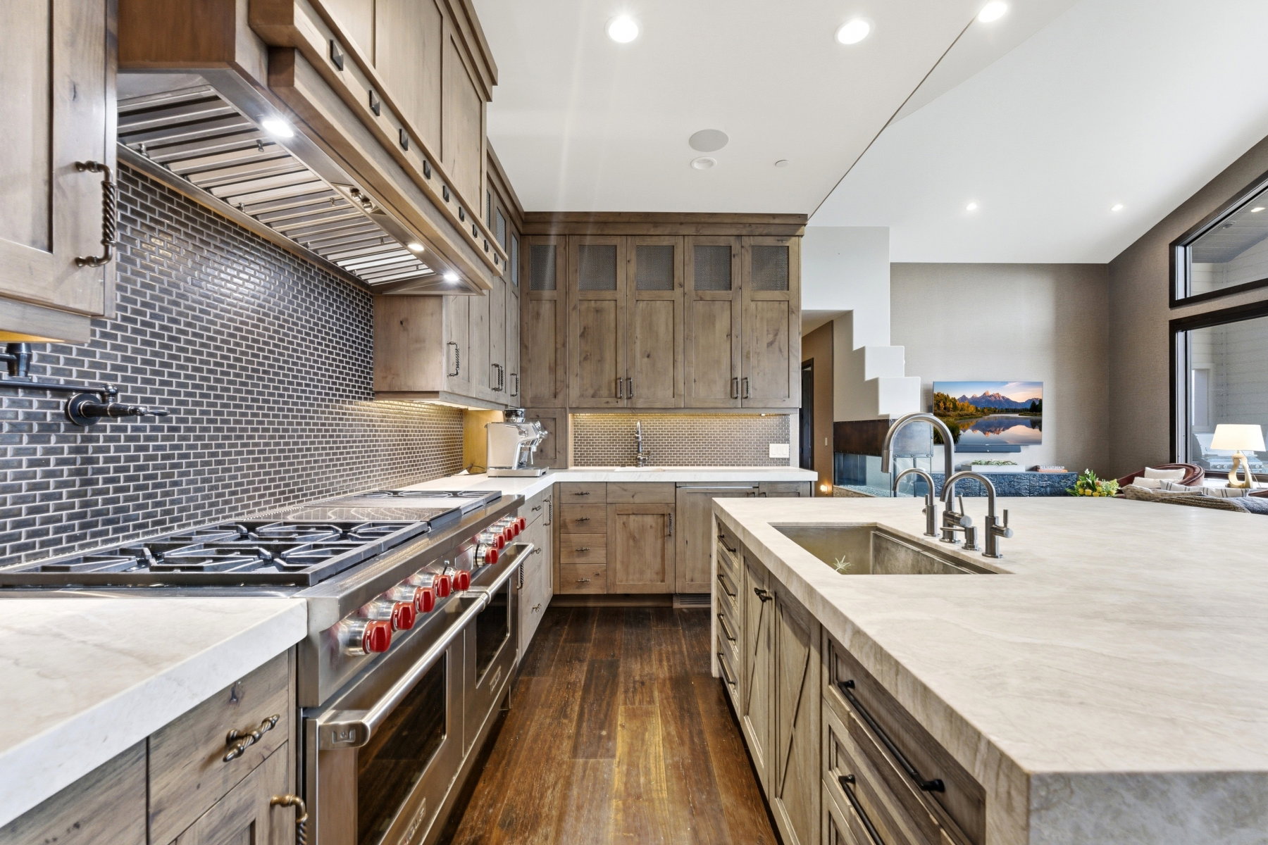 Gourmet kitchen featuring a substantial island with an undermount sink, stainless steel appliances including a range with griddle, wood-finish cabinetry, and a subway tile backsplash