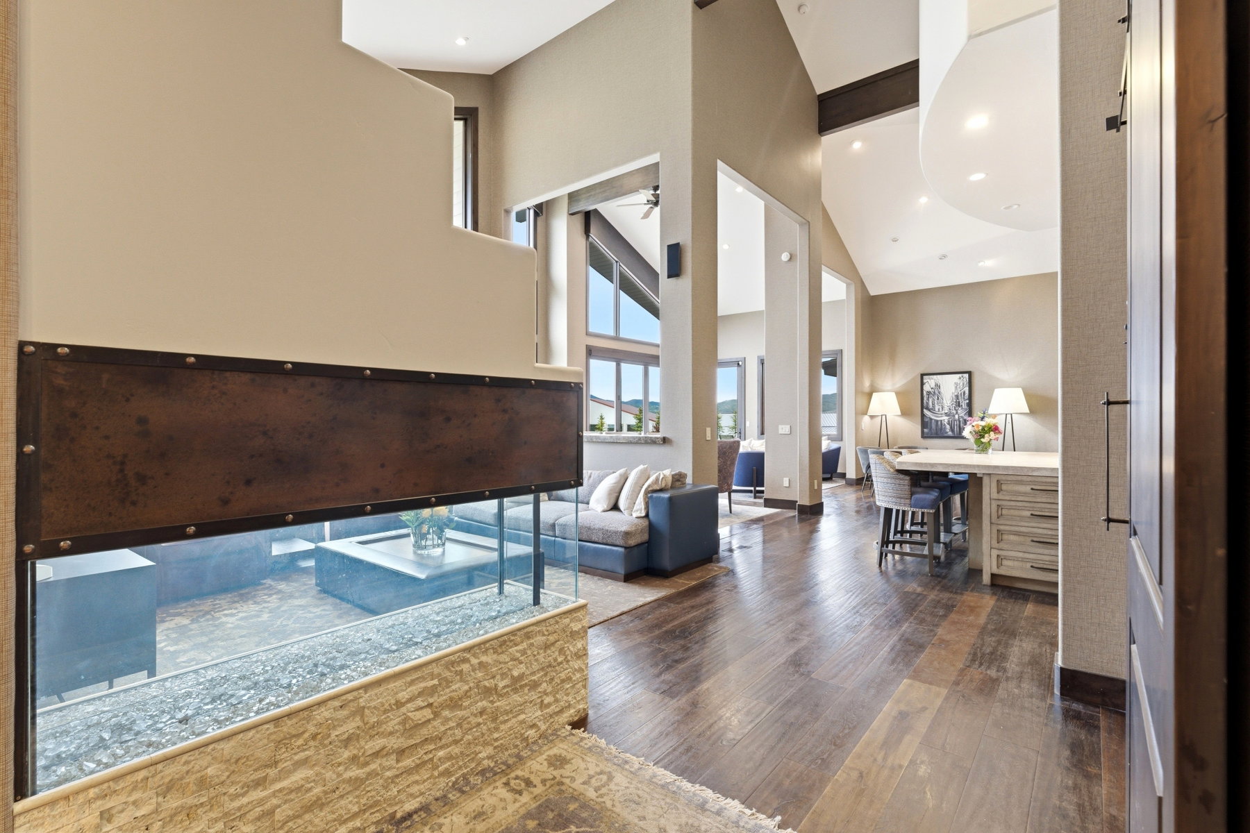 Open-concept living space featuring wood-finish flooring, vaulted ceilings, and large windows