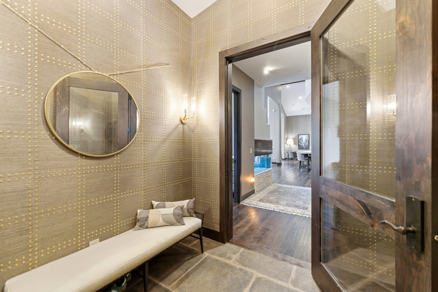 Entryway featuring patterned wall covering with metallic accents, a round wall-mounted mirror, and stone flooring