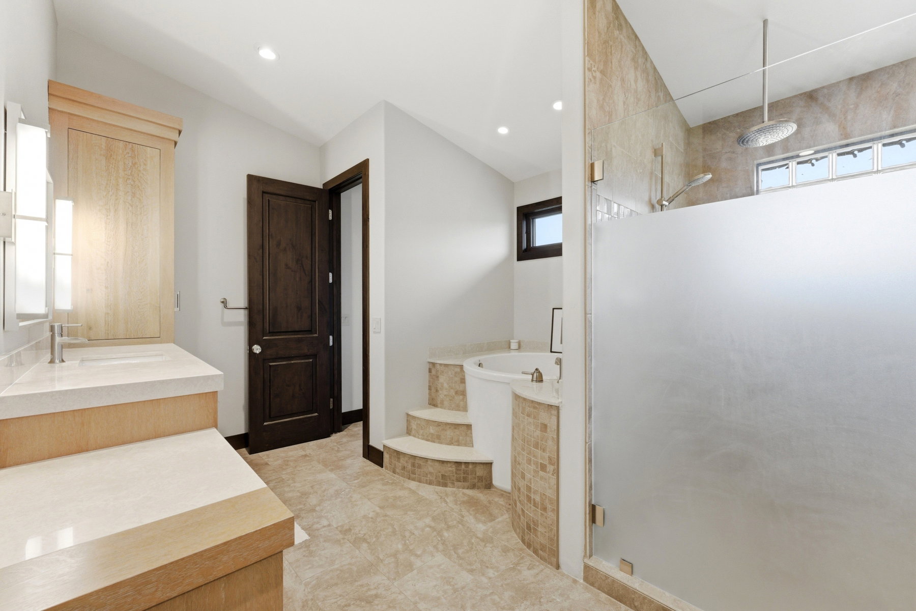 Bathroom featuring a step-up jetted tub with mosaic tile surround, a frosted glass shower enclosure with a rainfall showerhead, and a vanity with dual sinks and light-toned countertops