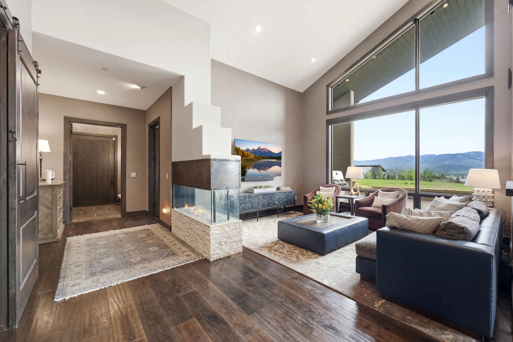 Spacious living area featuring expansive windows, vaulted ceilings, and dark wood-finish flooring