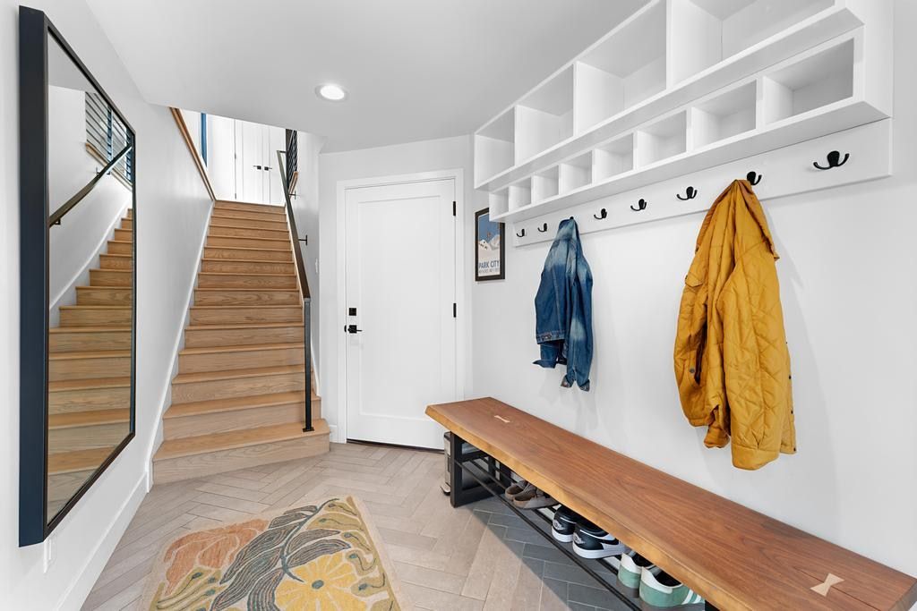 Entryway featuring herringbone wood-finish flooring, a built-in storage system with cubbies and coat hooks, a built-in wood bench with shoe storage, a light wood staircase with black metal railings, and a full-length wall mirror