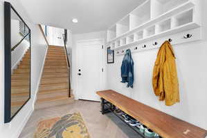 Entryway featuring herringbone wood-finish flooring, a built-in storage system with cubbies and coat hooks, a built-in wood bench with shoe storage, a light wood staircase with black metal railings, and a full-length wall mirror