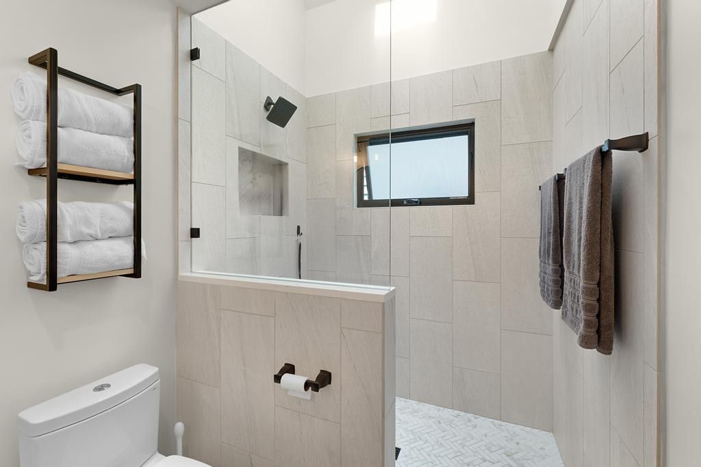 Walk-in shower with full glass enclosure, light-toned wall tiling, built-in shower niche, and a contrasting dark-framed window