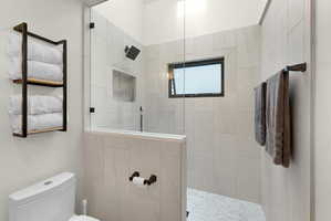 Walk-in shower with full glass enclosure, light-toned wall tiling, built-in shower niche, and a contrasting dark-framed window