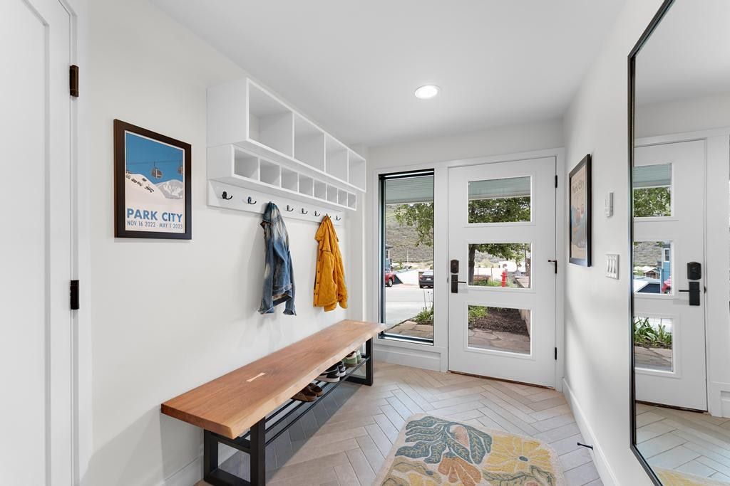 Entryway featuring a white built-in storage unit with cubbies and hooks, a natural wood bench with a black metal base, and light wood-finish flooring in a herringbone pattern