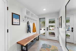 Entryway featuring a white built-in storage unit with cubbies and hooks, a natural wood bench with a black metal base, and light wood-finish flooring in a herringbone pattern