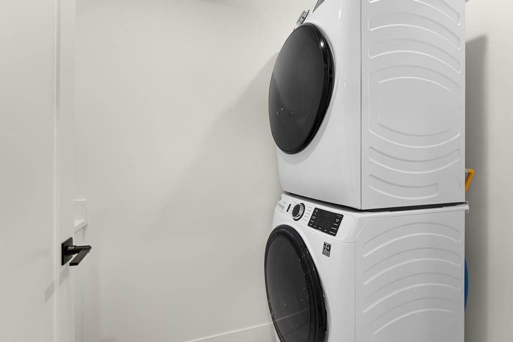 Dedicated laundry area featuring a white stackable washer and dryer unit, white walls, and a modern black door handle