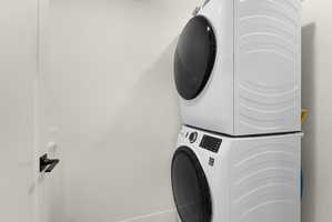 Dedicated laundry area featuring a white stackable washer and dryer unit, white walls, and a modern black door handle