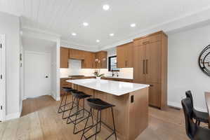 Modern kitchen featuring a large center island with a white countertop, wood-finish cabinetry, integrated paneled refrigerator, wood-finish flooring, and a paneled ceiling with recessed lighting