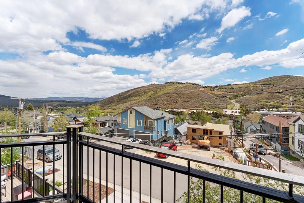 Balcony with black metal railings overlooking a mountainous landscape, residential properties, and a street
