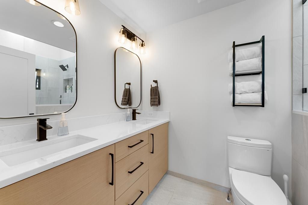 Bathroom featuring a dual vanity with light wood-finish cabinetry, white countertops, and matte black hardware