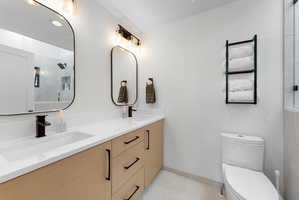 Bathroom featuring a dual vanity with light wood-finish cabinetry, white countertops, and matte black hardware