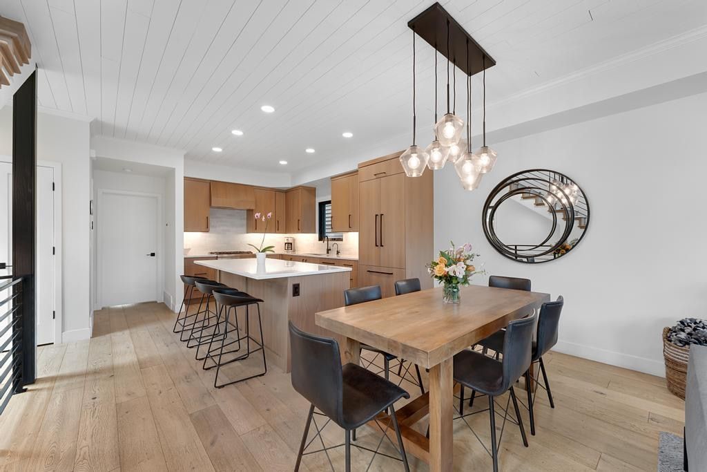 Contemporary open-concept kitchen and dining area featuring wood-finish flooring, a kitchen island with seating, integrated appliances, and a planked ceiling