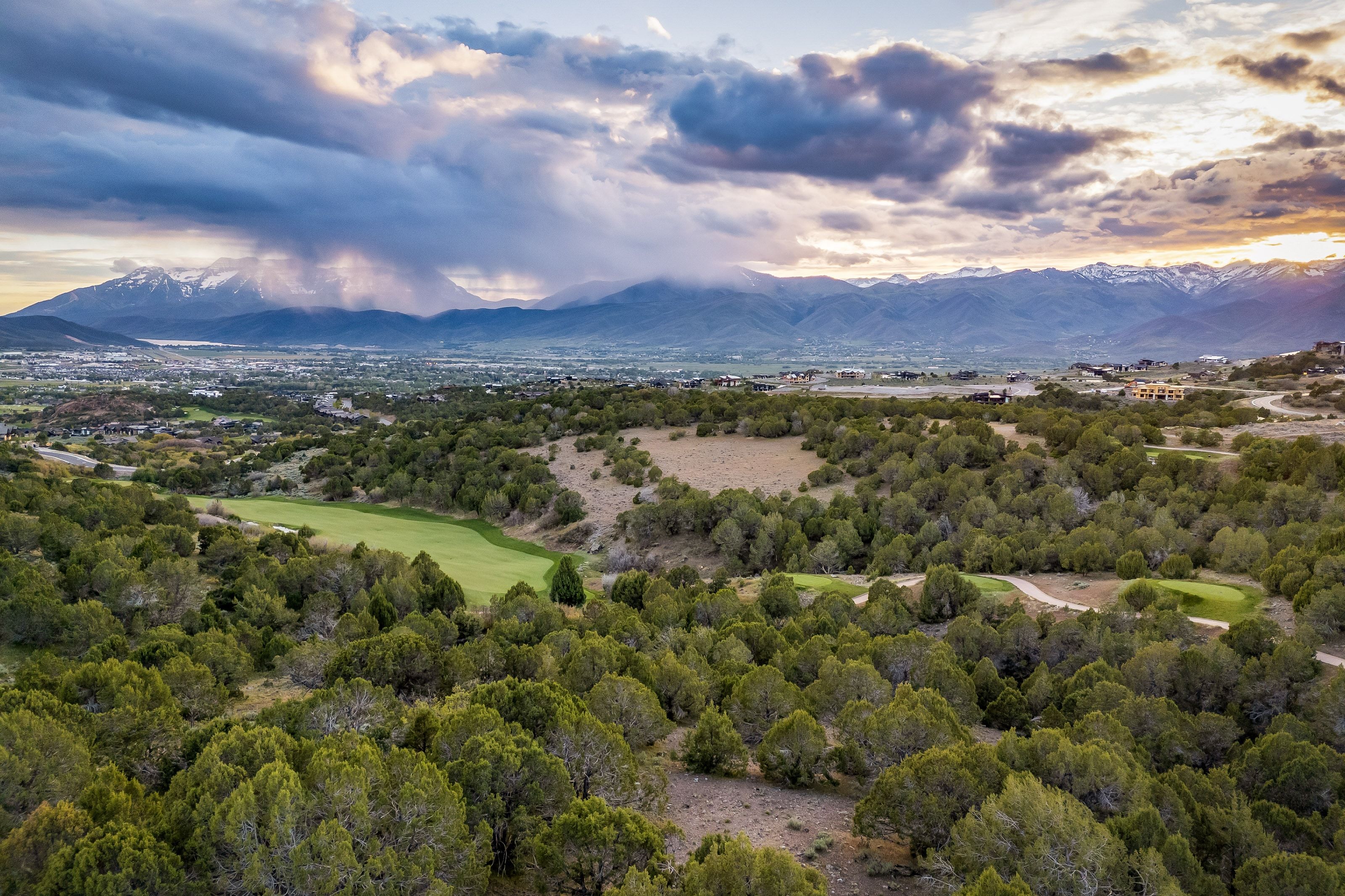 Expansive landscape with a golf course fairway, surrounded by abundant natural foliage, distant mountain range backdrop, and scattered residential properties