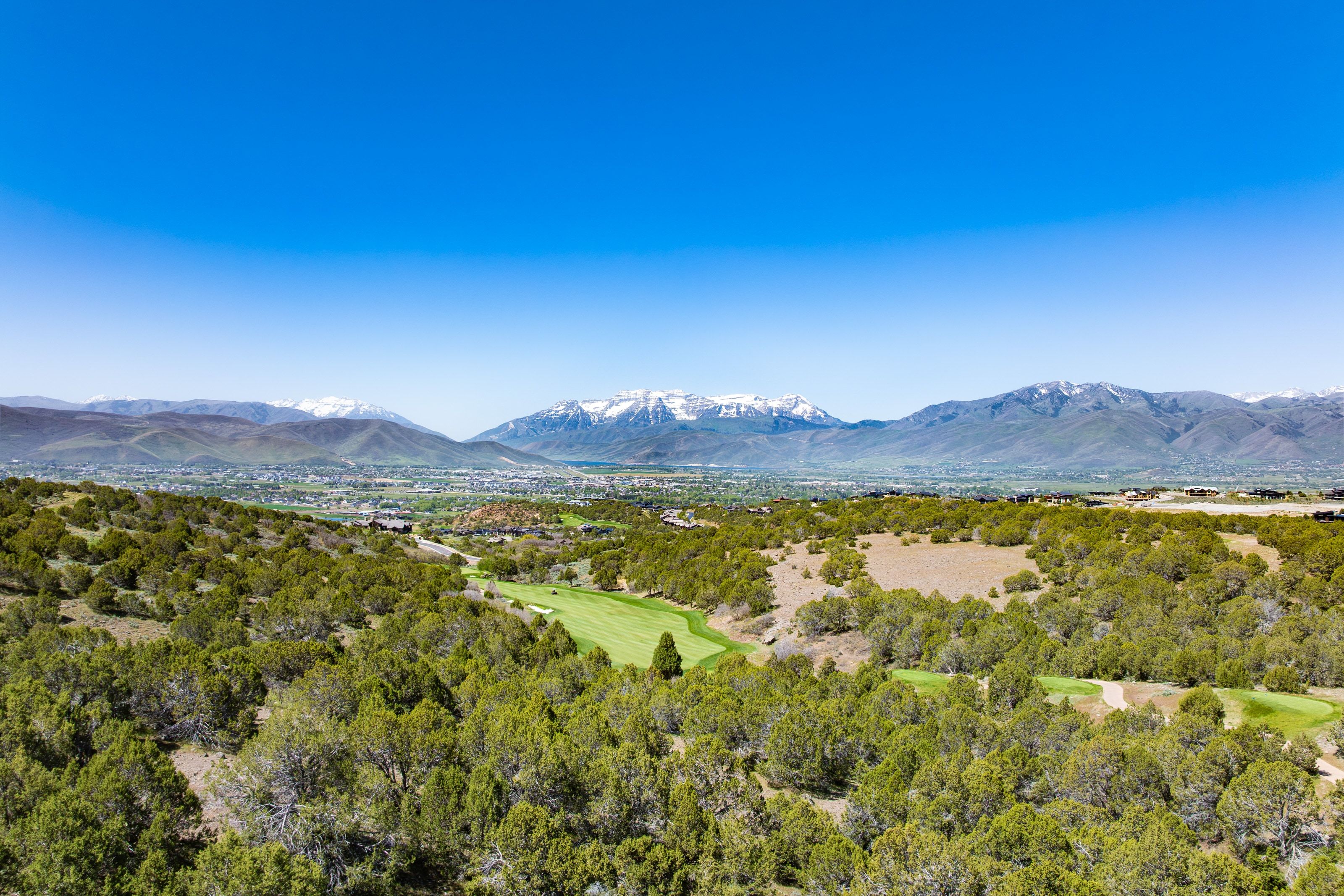 Expansive golf course property featuring a lush green fairway, natural landscape with numerous trees, and distant snow-capped mountains