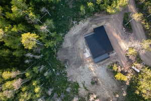 Modern cabin featuring a dark metal roof, surrounded by mature trees, with a gravel driveway and surrounding cleared land
