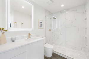 Contemporary bathroom featuring a floating white vanity with an integrated sink and gold-tone faucet, an illuminated rectangular mirror, and a frameless glass shower enclosure with white marble-look wall tiles and built-in shelving
