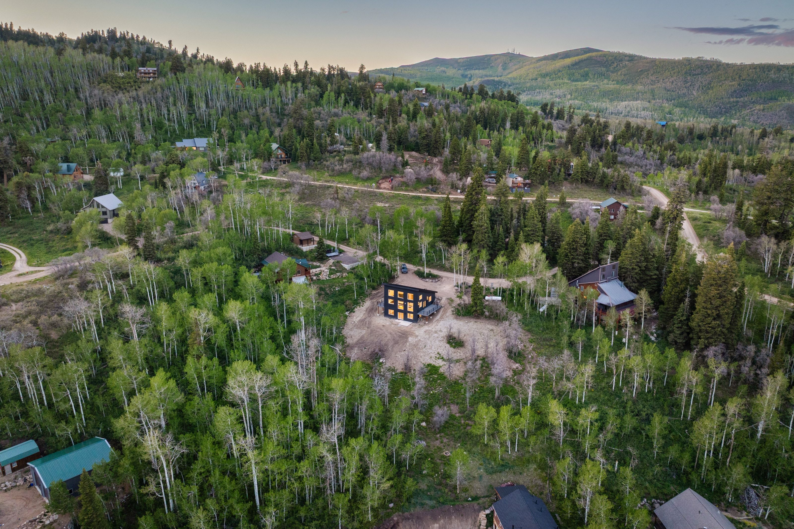 Mountainous landscape featuring abundant evergreen and deciduous trees, with multiple properties nestled amongst the foliage