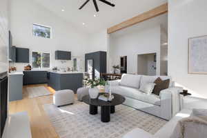 Open-concept living area featuring high vaulted ceilings, light wood-finish flooring, and a prominent exposed beam