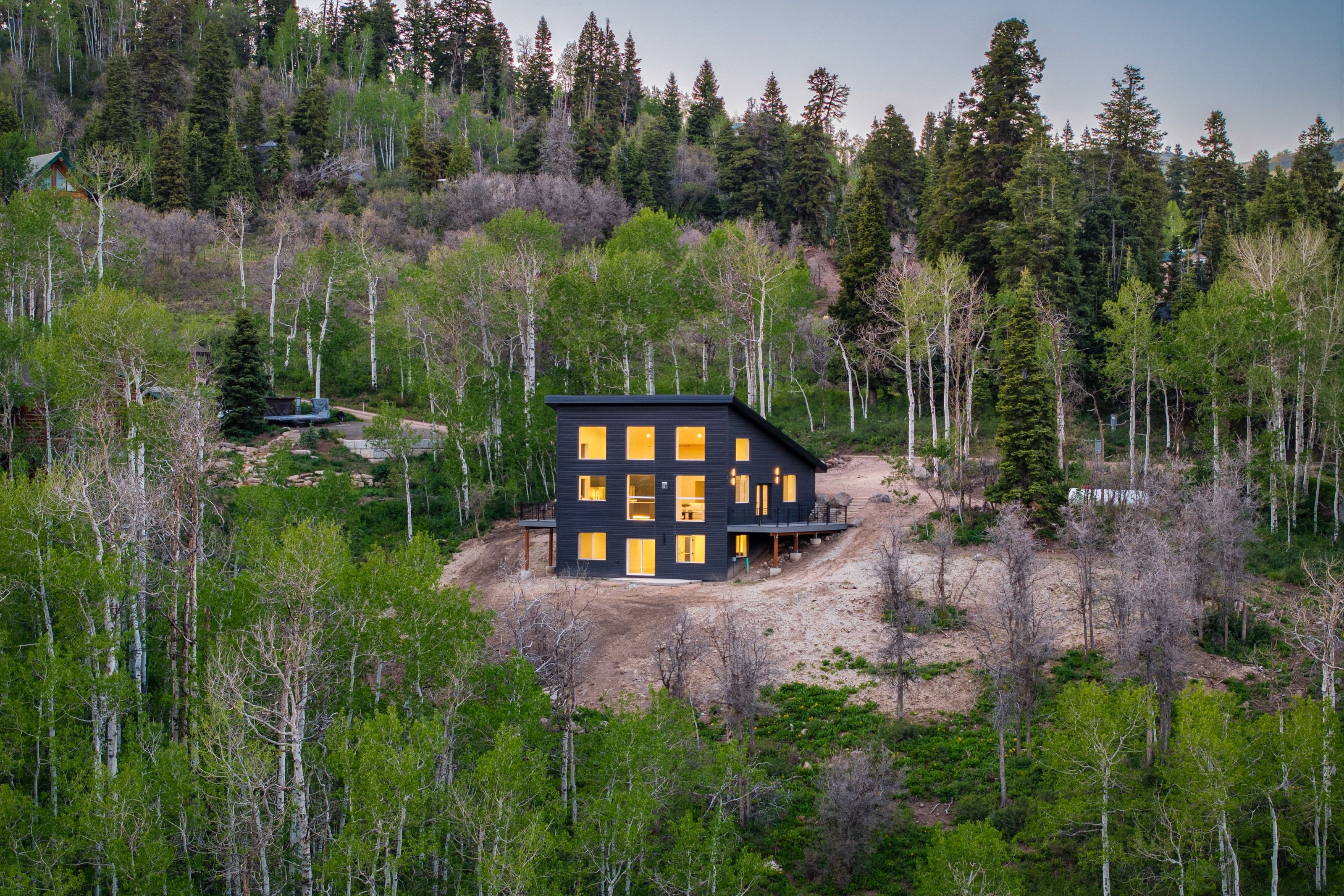 Modern black-clad residence featuring a sloped roofline, multiple square windows, and a raised exterior deck