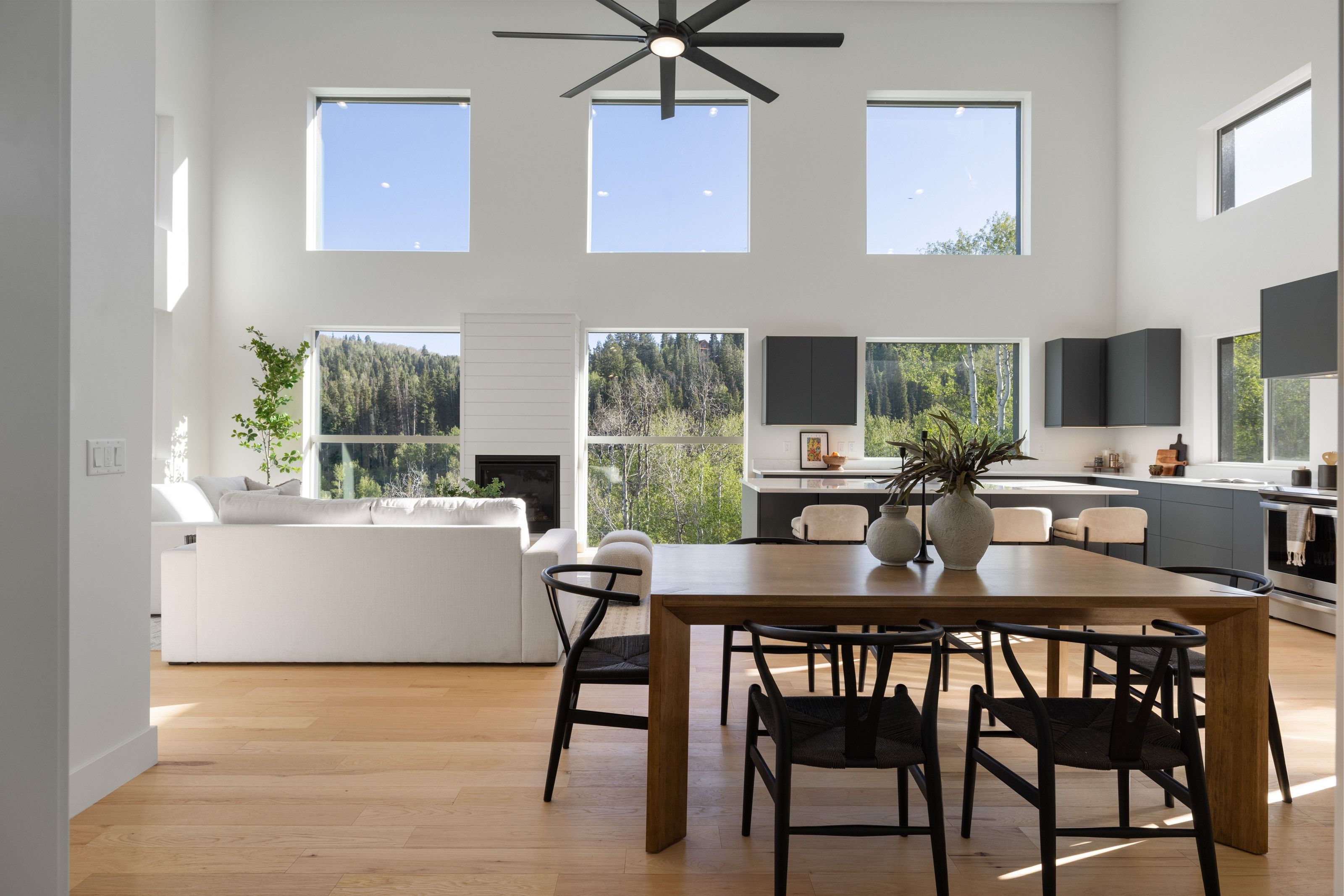 Open-concept living space featuring high ceilings, wood-finish flooring, a modern fireplace, and a kitchen with dark cabinetry and light countertops