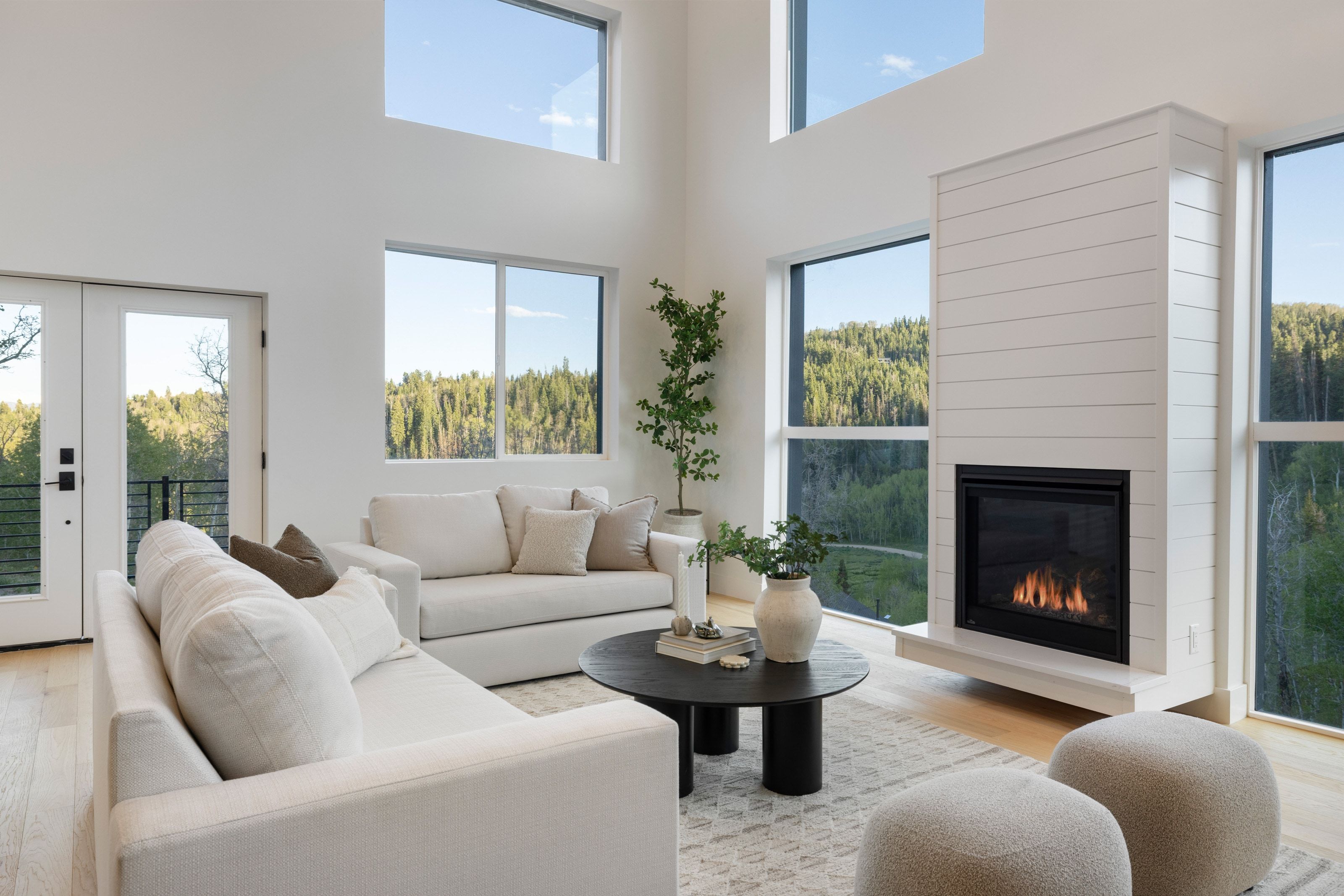 Vaulted ceiling living area featuring a shiplap-clad fireplace, light wood-finish flooring, full-light French doors, and expansive windows