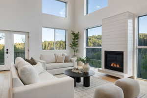 Vaulted ceiling living area featuring a shiplap-clad fireplace, light wood-finish flooring, full-light French doors, and expansive windows