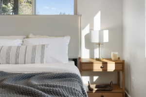 Bedroom featuring a large window, light-colored walls, and a wooden nightstand with a drawer