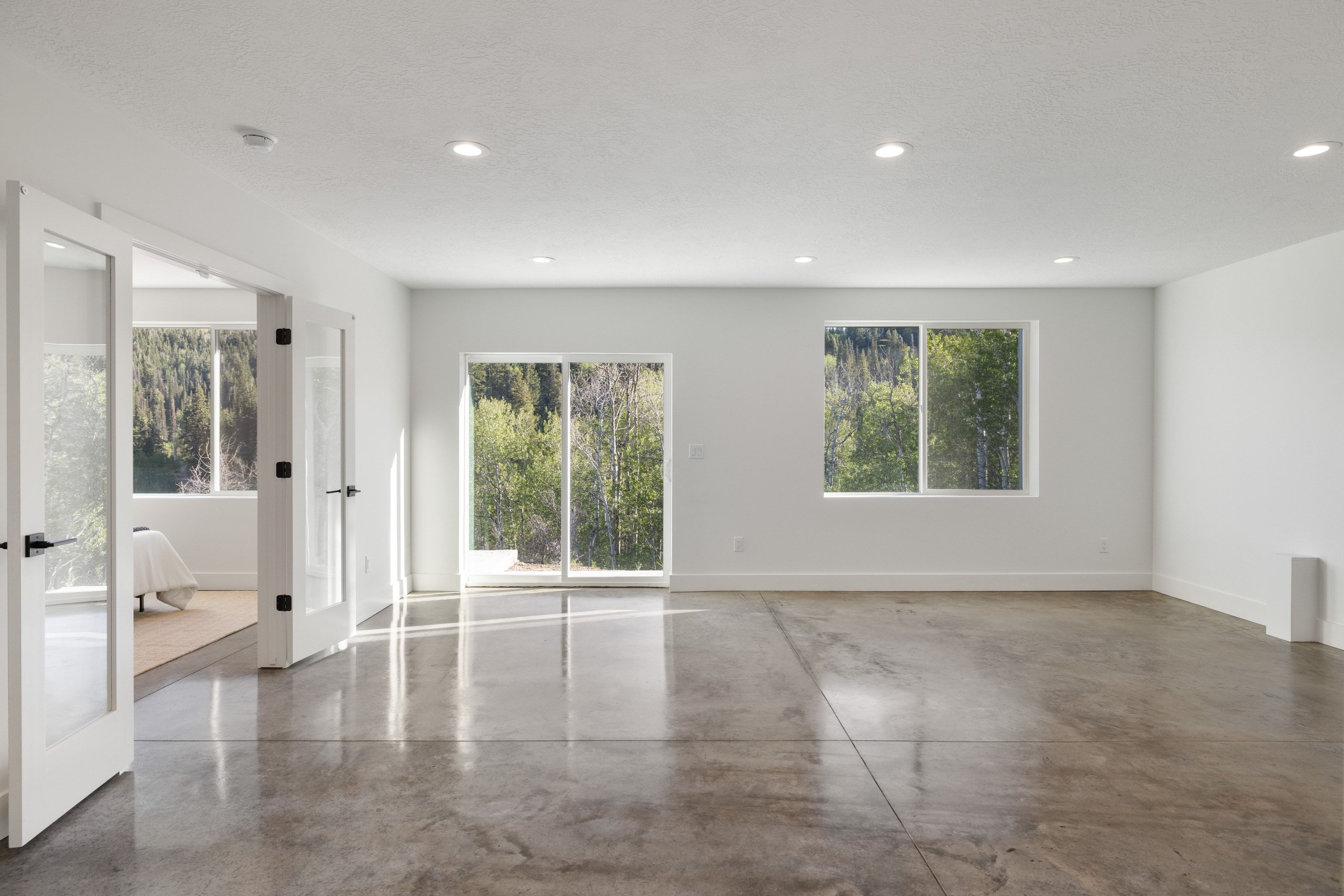 Spacious room featuring polished concrete flooring, recessed lighting, white walls, a large sliding glass door, and an additional window