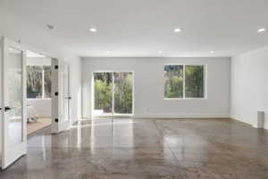 Spacious room featuring polished concrete flooring, recessed lighting, white walls, a large sliding glass door, and an additional window