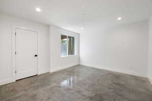 Spacious room featuring polished concrete flooring, recessed lighting, a contemporary two-panel door with matte black hardware, and a window providing natural illumination