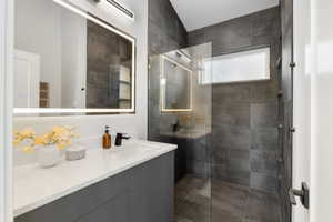 Contemporary bathroom featuring a grey vanity with a white countertop, an illuminated mirror, and a walk-in shower with dark grey tile surrounds and a glass enclosure