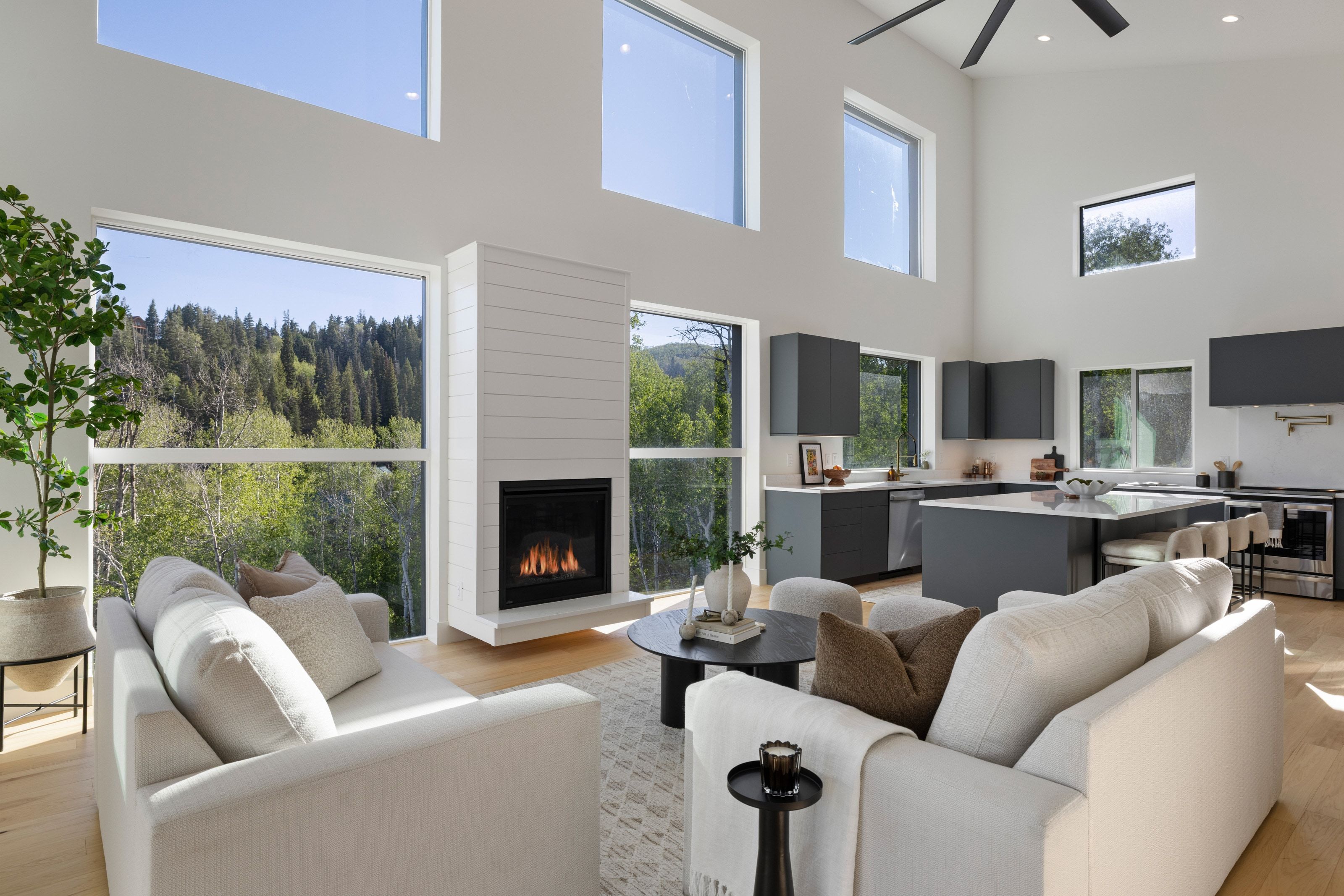 Vaulted ceilings with abundant natural light, a contemporary fireplace with shiplap-style surround, a modern kitchen featuring dark cabinetry and a central island, and wood-finish flooring throughout