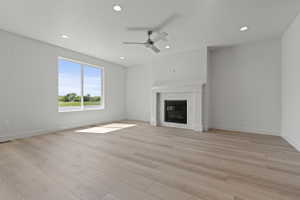 Spacious room featuring light wood-finish flooring, a contemporary fireplace with a decorative tile surround and mantel, a ceiling fan, recessed lighting, and a large window providing ample natural light and a green landscape backdrop