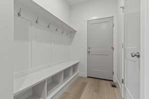 Entryway featuring light wood-finish flooring, white built-in storage bench with cubbies, white wainscoting with coat hooks, and a gray panel door with brushed nickel hardware