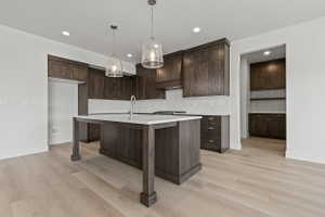 Kitchen featuring wood-finish flooring, dark wood cabinetry, and a white tile backsplash