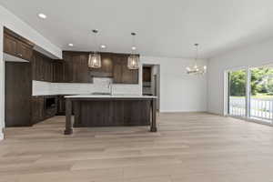 Spacious kitchen and living area featuring wood-finish flooring, dark wood cabinetry, and a kitchen island with a light-colored countertop