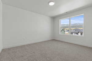 Spacious room featuring a large window with mountain scenery, neutral carpeting, white baseboards, and a flush-mount ceiling light fixture