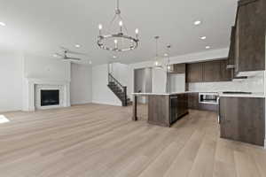 Open-concept living space featuring light wood-finish flooring throughout, a modern gas fireplace with a white mantel and tile surround, and a kitchen with dark wood cabinetry and white countertops